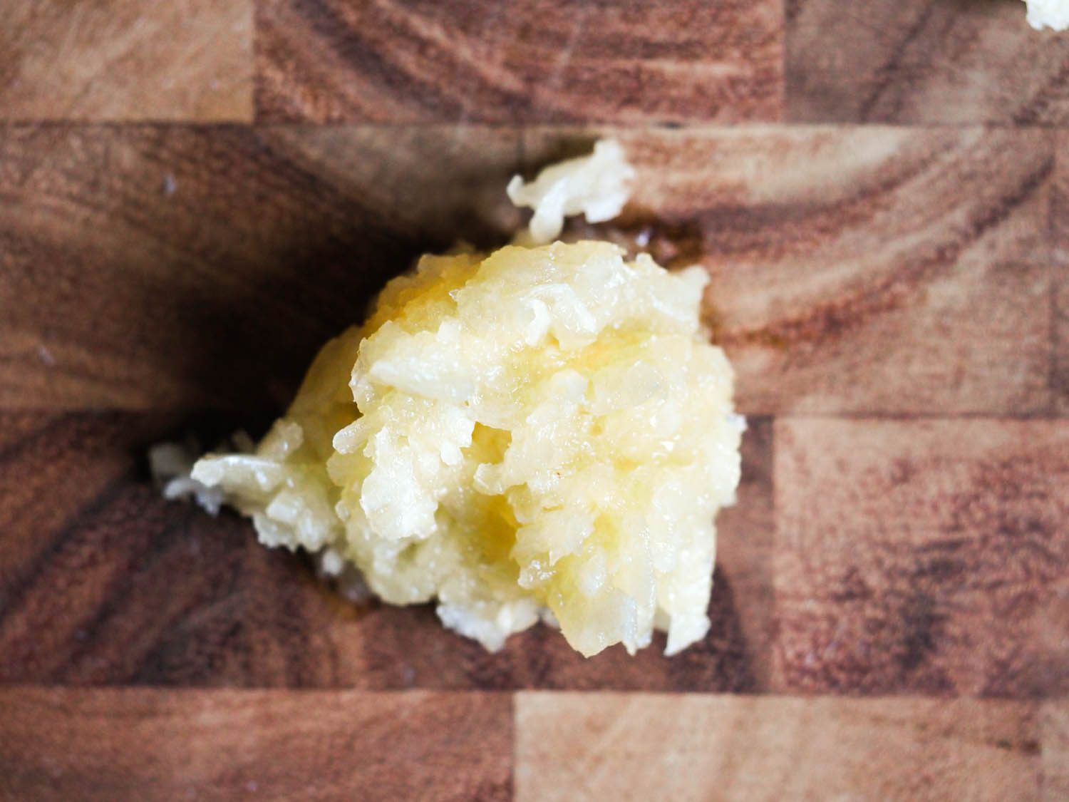 A pile of crushed garlic on a cutting board.