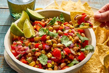 A bowl of cowboy caviar surrounded by tortilla chips with a hand holding a chip topped with the dish