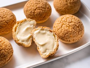 Six choux au craquelins on a white platter with one of them cut in half.