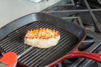A person testing the temperature of a pork chop being cooked in the Cuisinart Chef's Classic 9.25-inch Square Grill Pan 