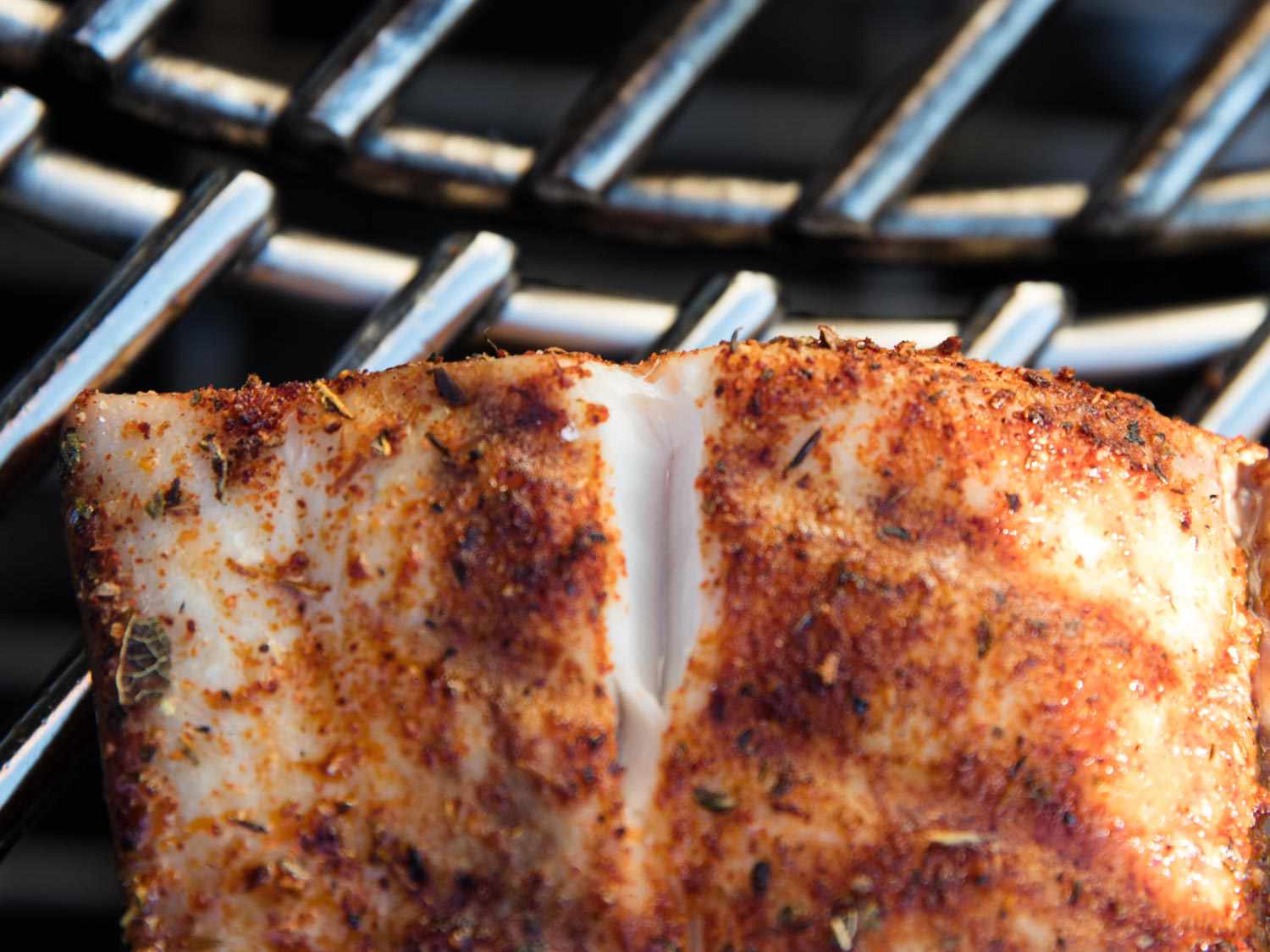 Close-up of a fish fillet on the grill. A split in the fillet reveals the interior, which is white and no longer opaque.