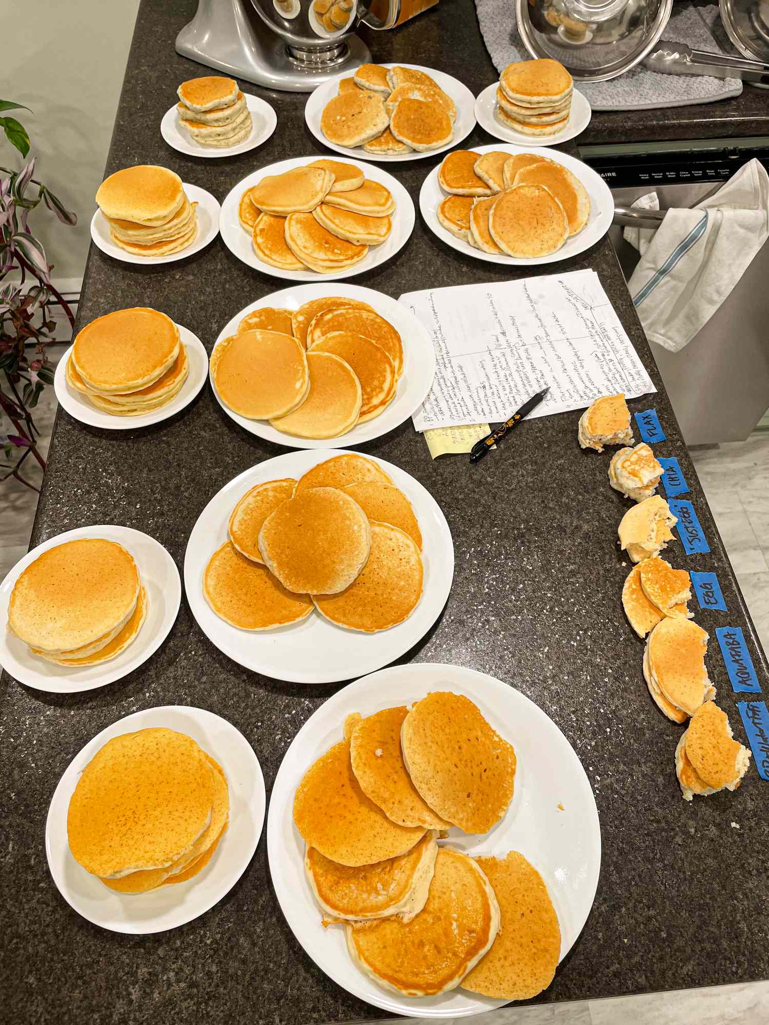 Several plates of pancakes arranged on a counter accompanied by a document and kitchen equipment visible in the background