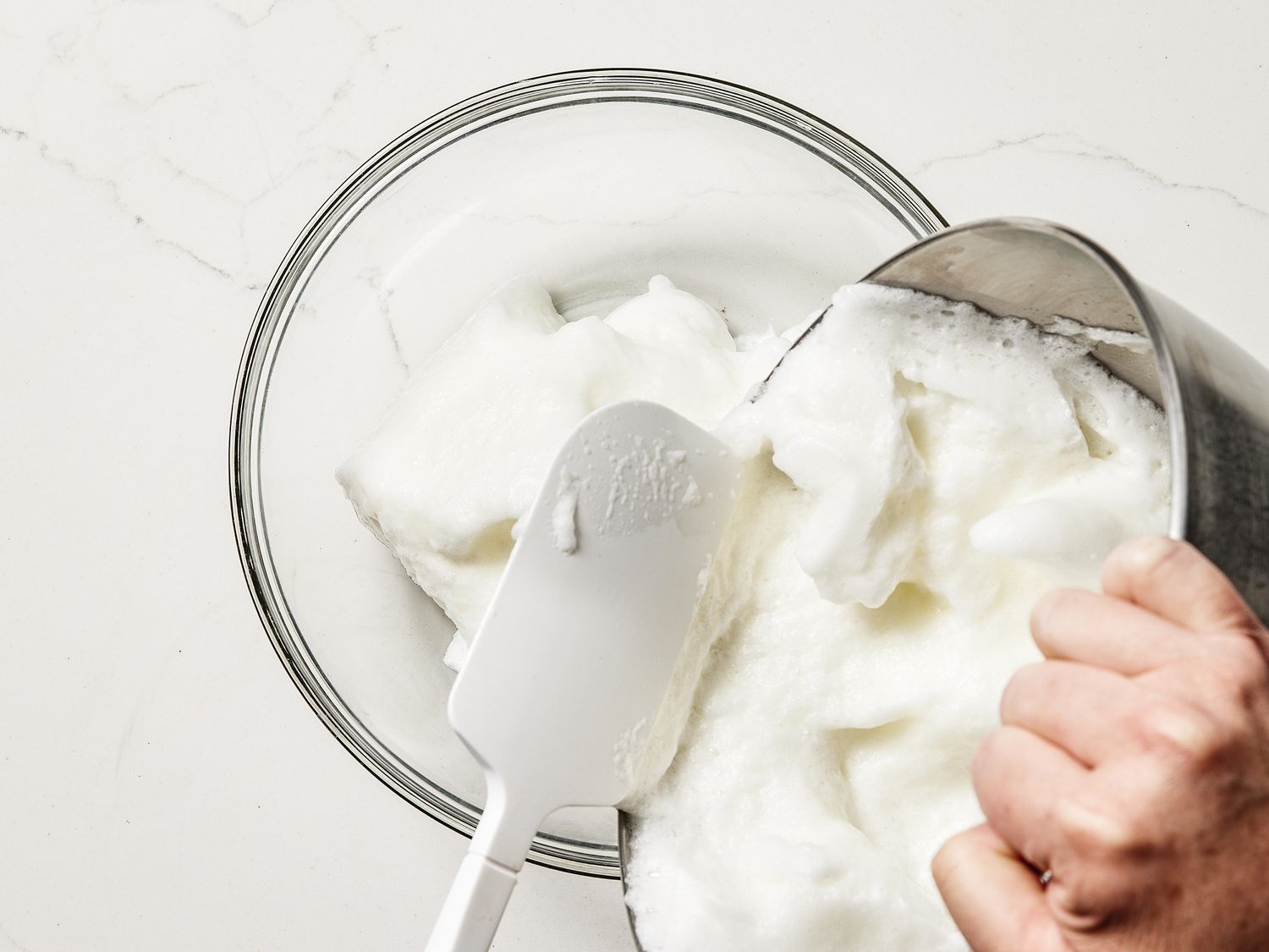 fluffed up egg whites being poured from stand mixer into glass bowl 