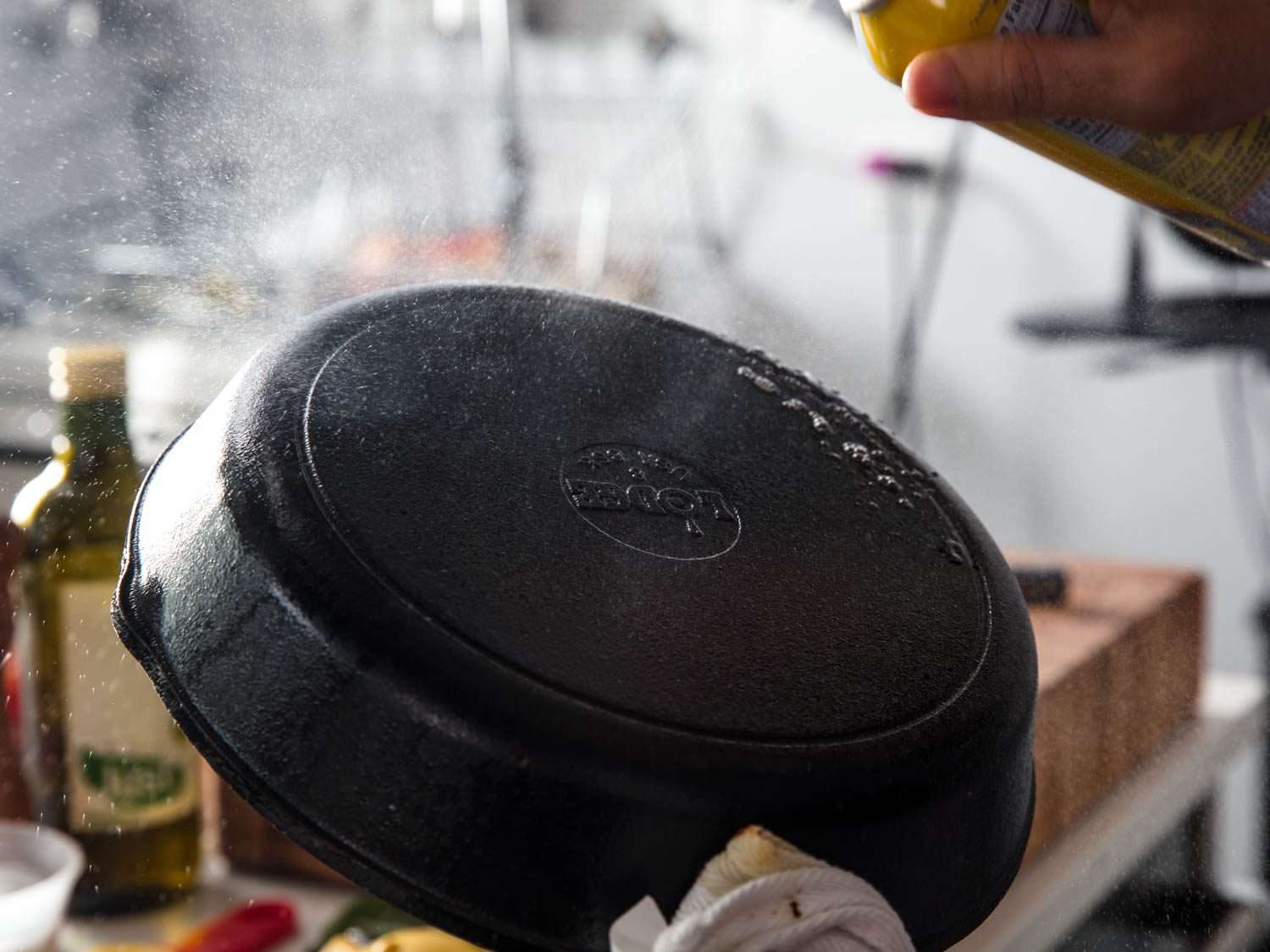 The bottom side of a cast iron skillet being sprayed with nonstick cooking spray.