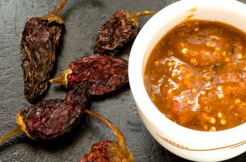 A small bowl of chile morita salsa next to some dried morita chiles. 