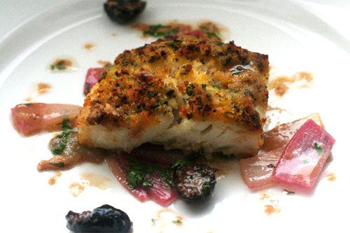 A baked piece of baked cod with breadcrumbs on a white plate.