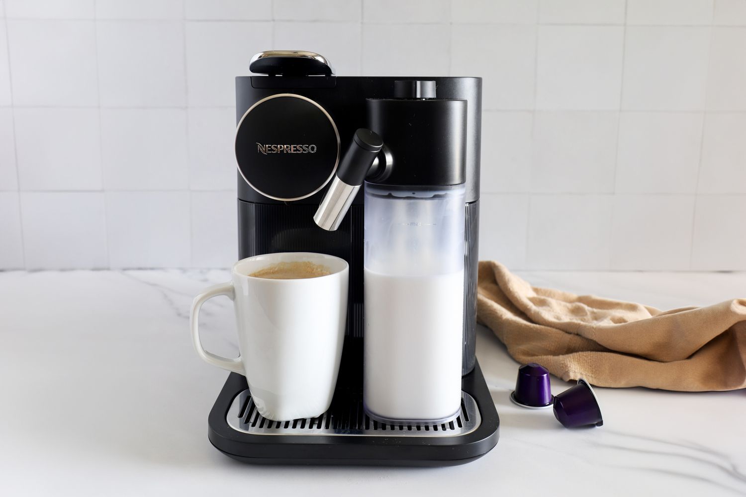 The Nespresso Gran Lattissima Original Espresso Machine by De’Longhi on a kitchen counter with a mug and a towel