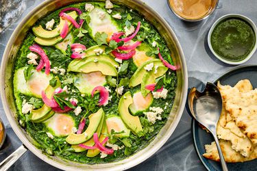 Pot of shakshuka on grey stone surface, with coffee cup, and side of pita. 