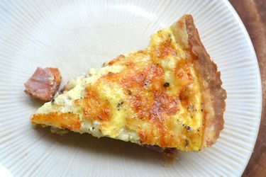 Overhead view of a slice of ham and cheese quiche served on a white plate.