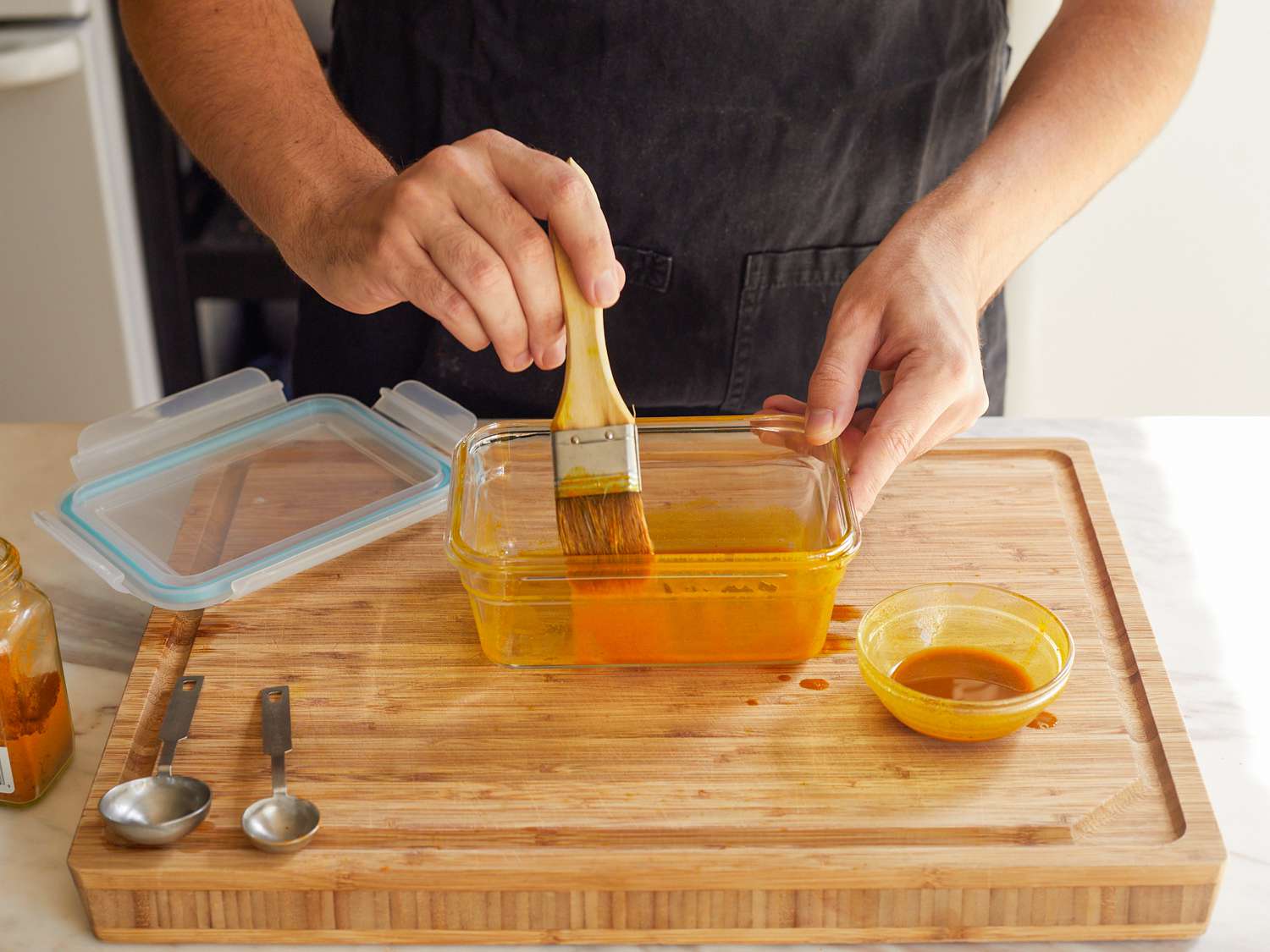 Hand brushing the sides of a Glasslock Rectangle Oven Safe Container with a turmeric mixture