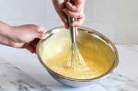 Hands whisking yellow batter in a Vollrath mixing bowl
