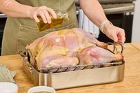 A person pouring olive oil onto a raw Grassland Beef Pasture Raised Turkey