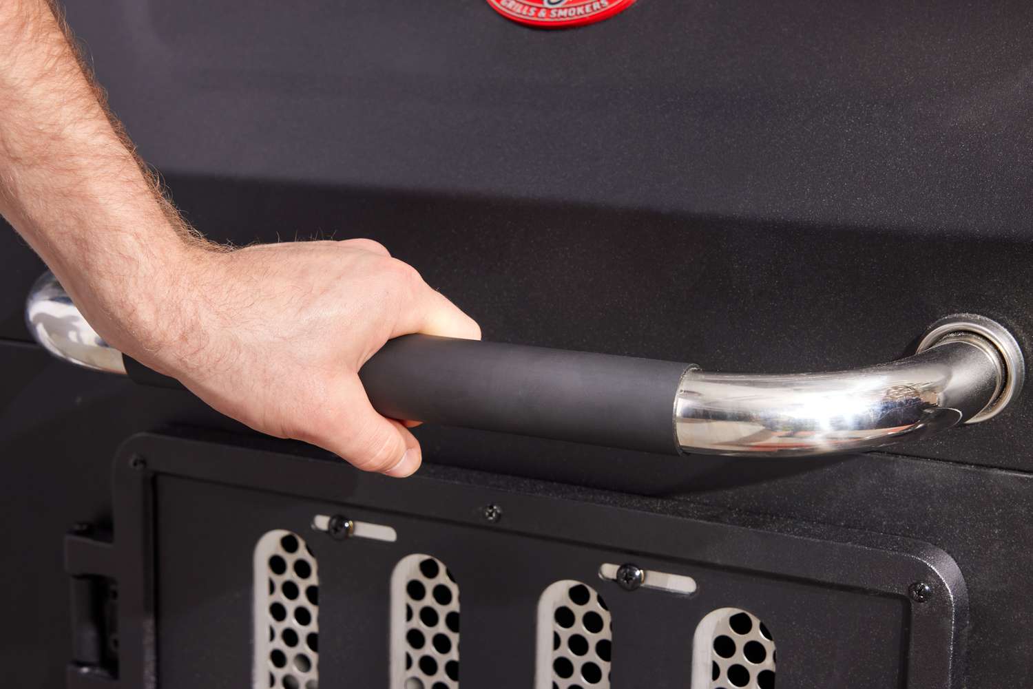 A hand on the handle of a charcoal grill