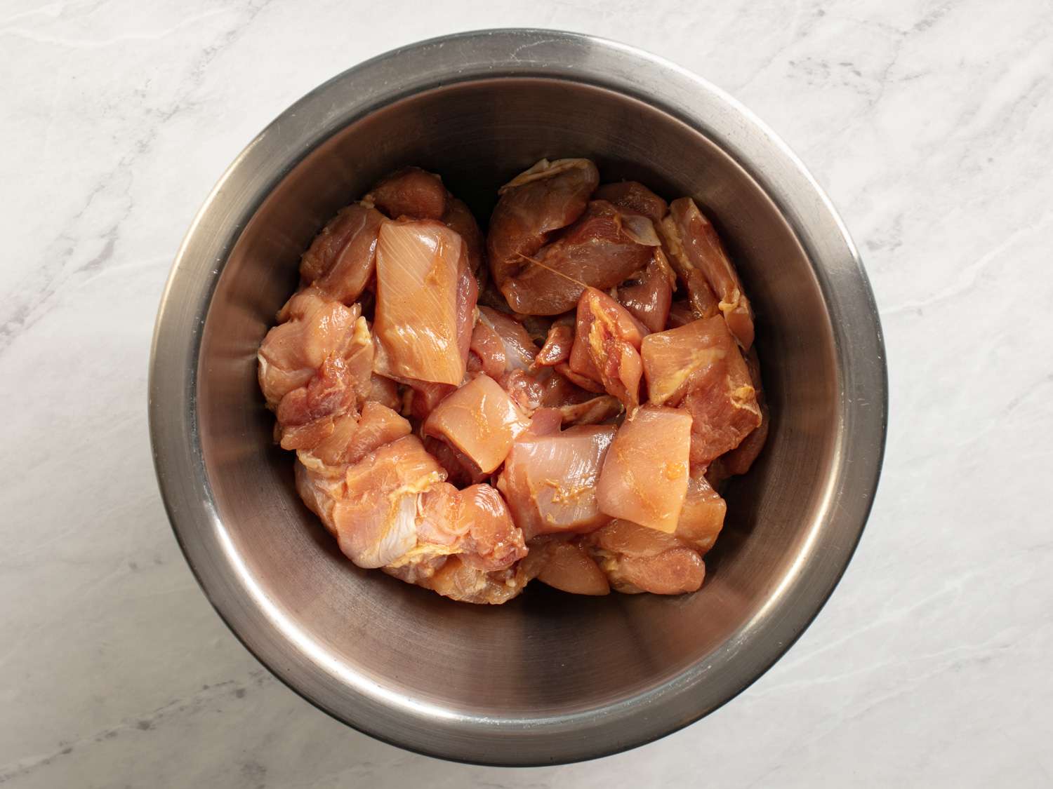 Chopped boneless, skinless chicken thighs coated in a kung pao marinade in a metal bowl.