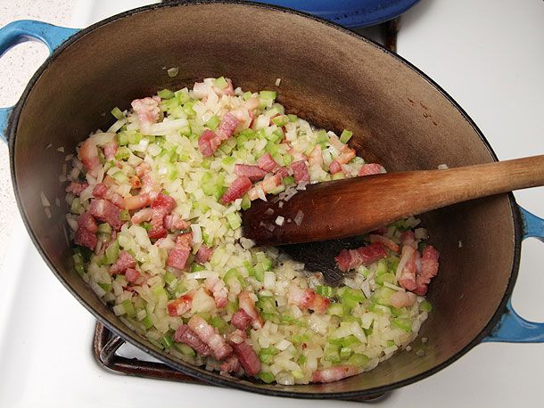 Adding celery and onions to browned salt pork in a Dutch oven. 