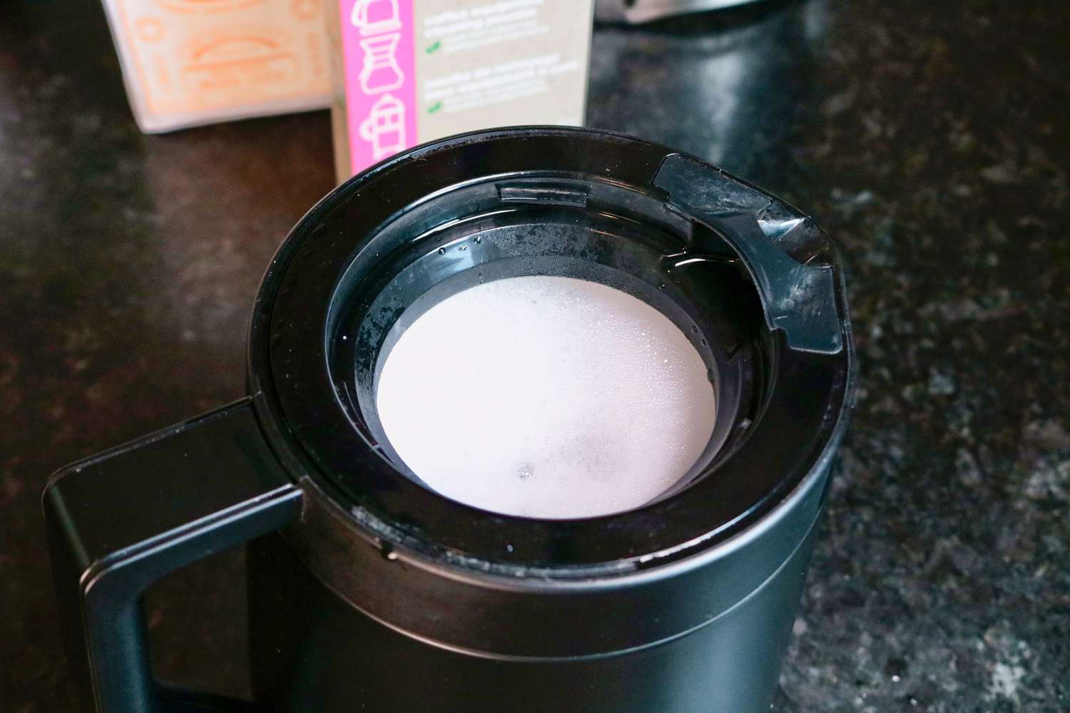 a coffee maker's carafe filled with foamy cleaning solution