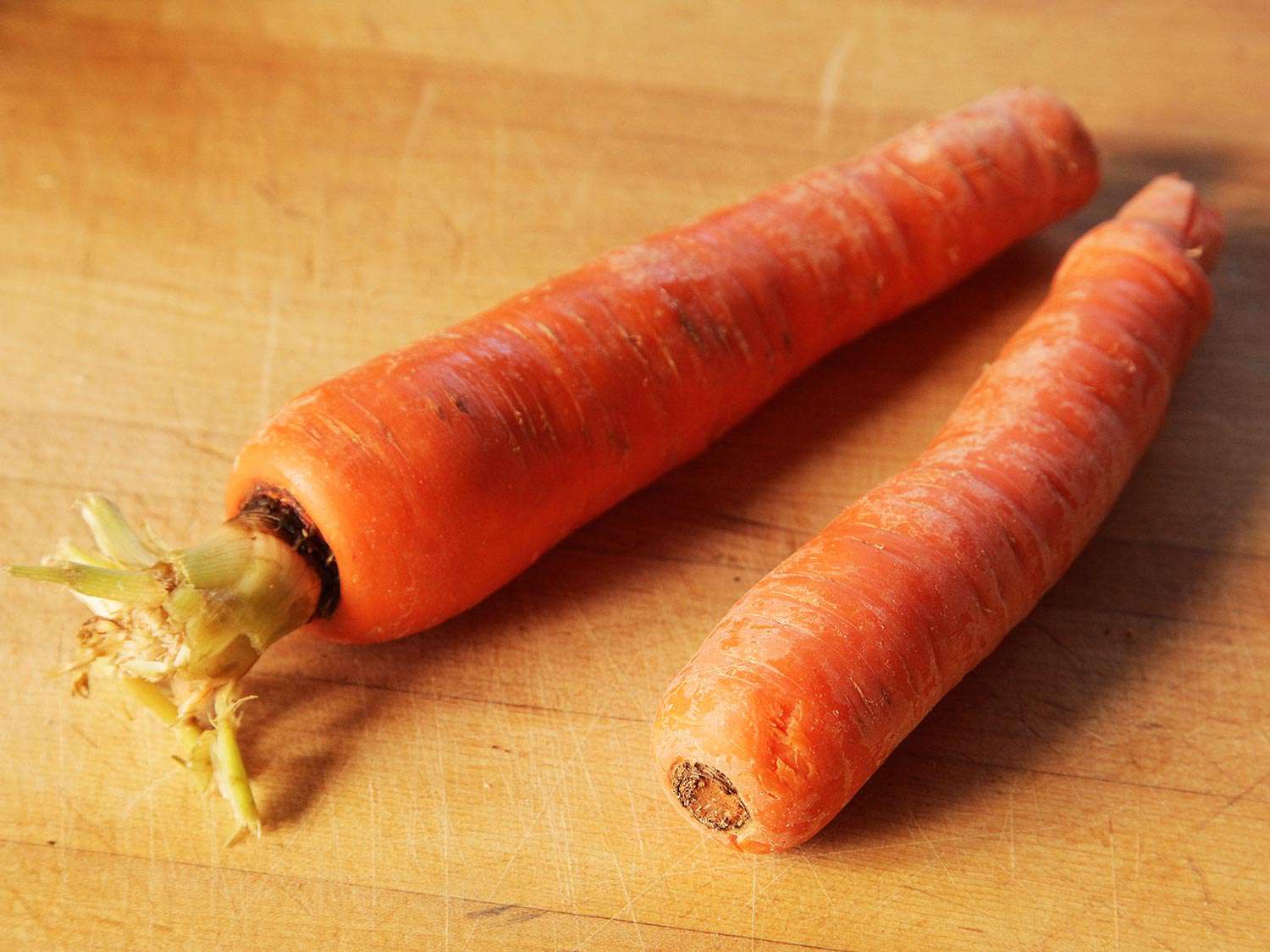 Two whole carrots on a wooden cutting board