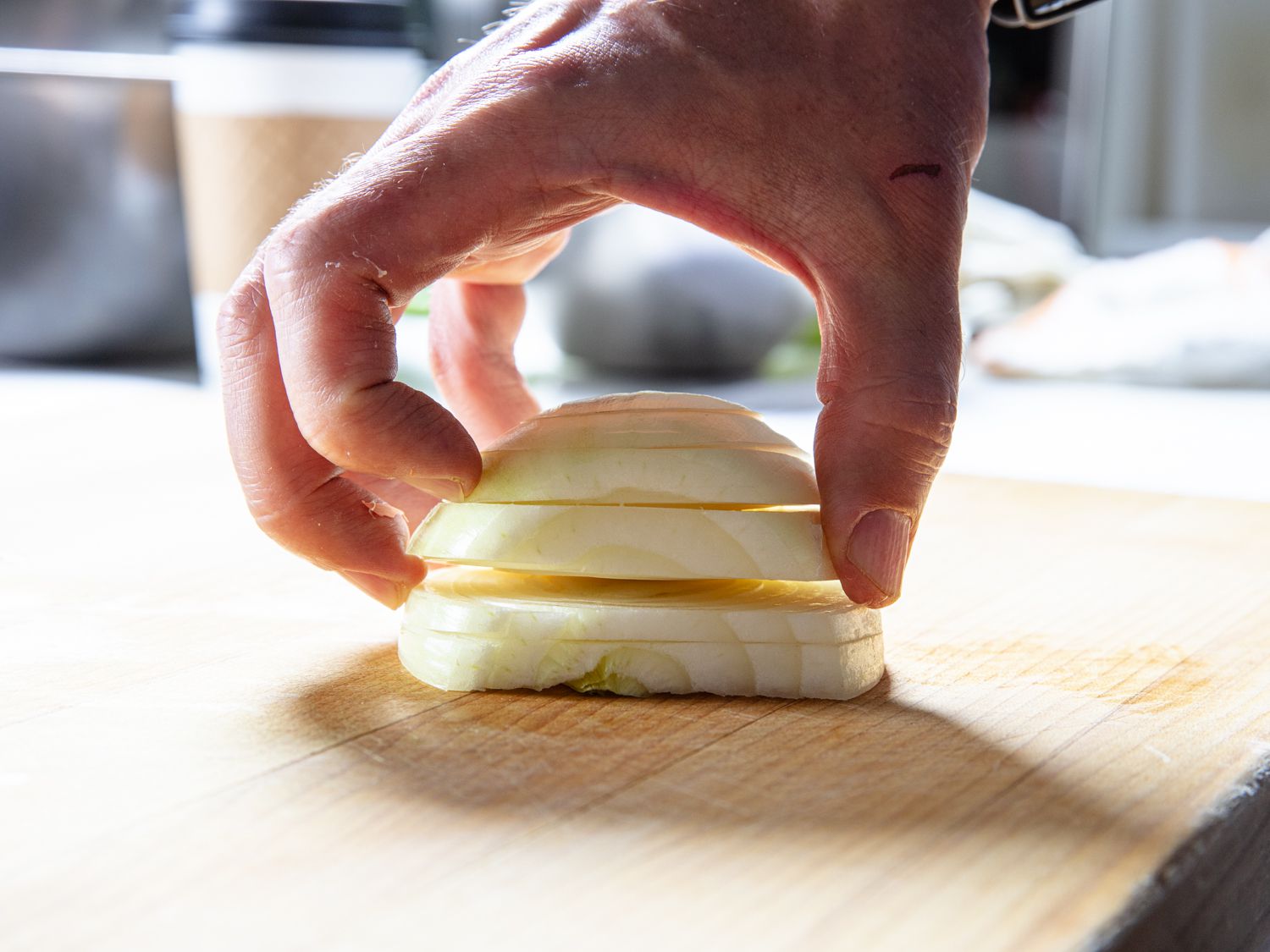 Hand splaying out cut layers of an onion that has been sliced along the Z-axis to illustrate how making more cuts results in a finer dice.