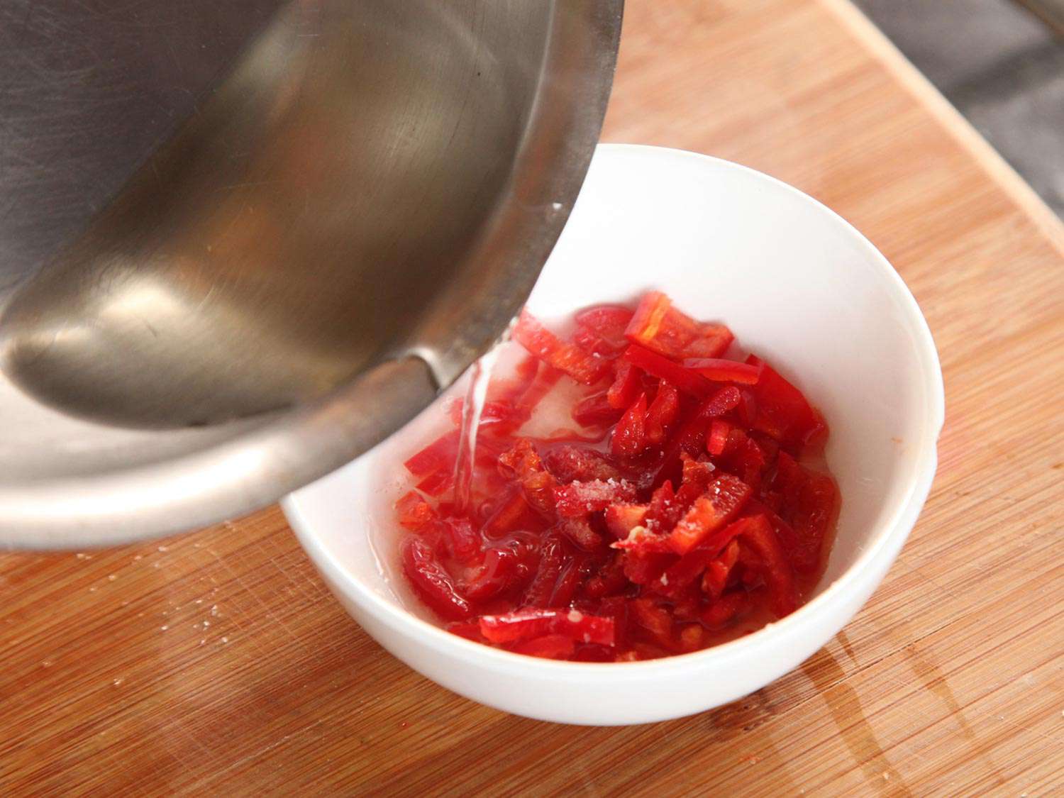 Pouring vinegar brine into a bowl of Thai chiles to pickle. 