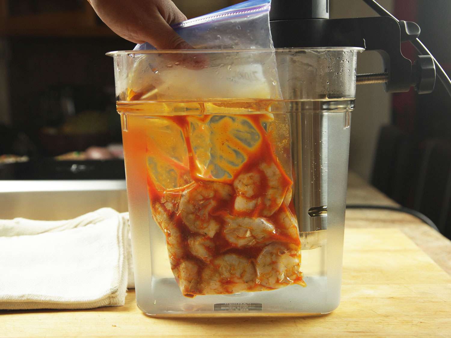 The sealed bag of shrimp and seasonings is lowered into a cambro container to cook sous vide.