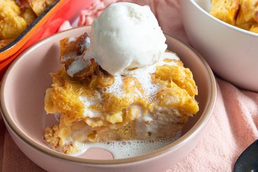 Soft pink bowl with bread pudding a la mode, on a soft pink textile, with a white bowl of bread pudding and full red tray of bread pudding on the sides. 