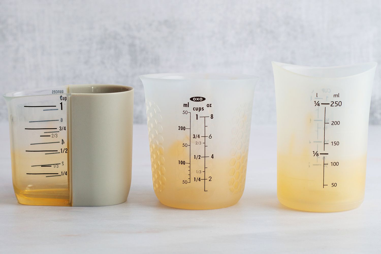 Three turmeric-stained measuring cups on a marble surface. 