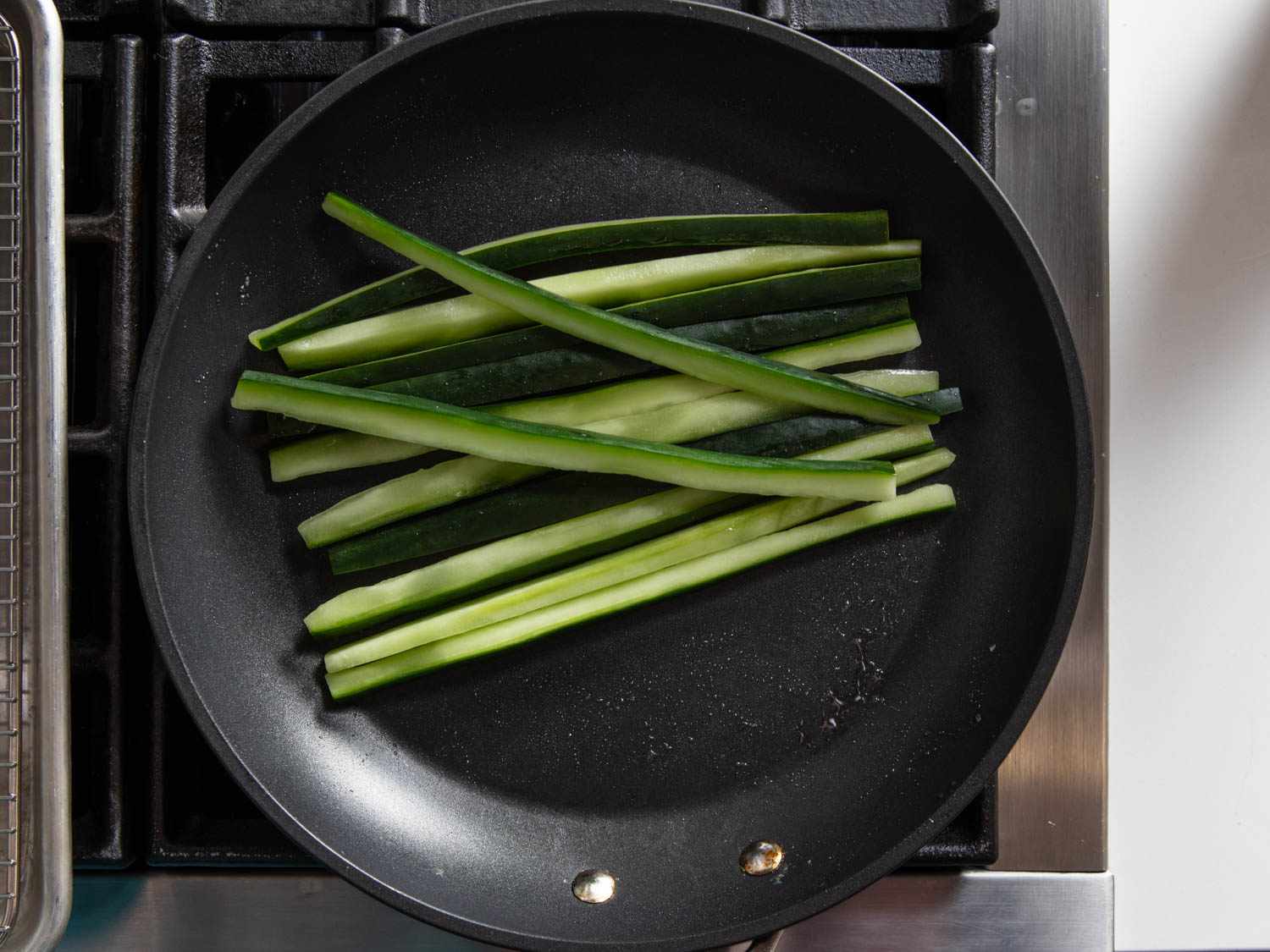 Long thin slices of cucumber in a nonstick skillet on a stovetop.