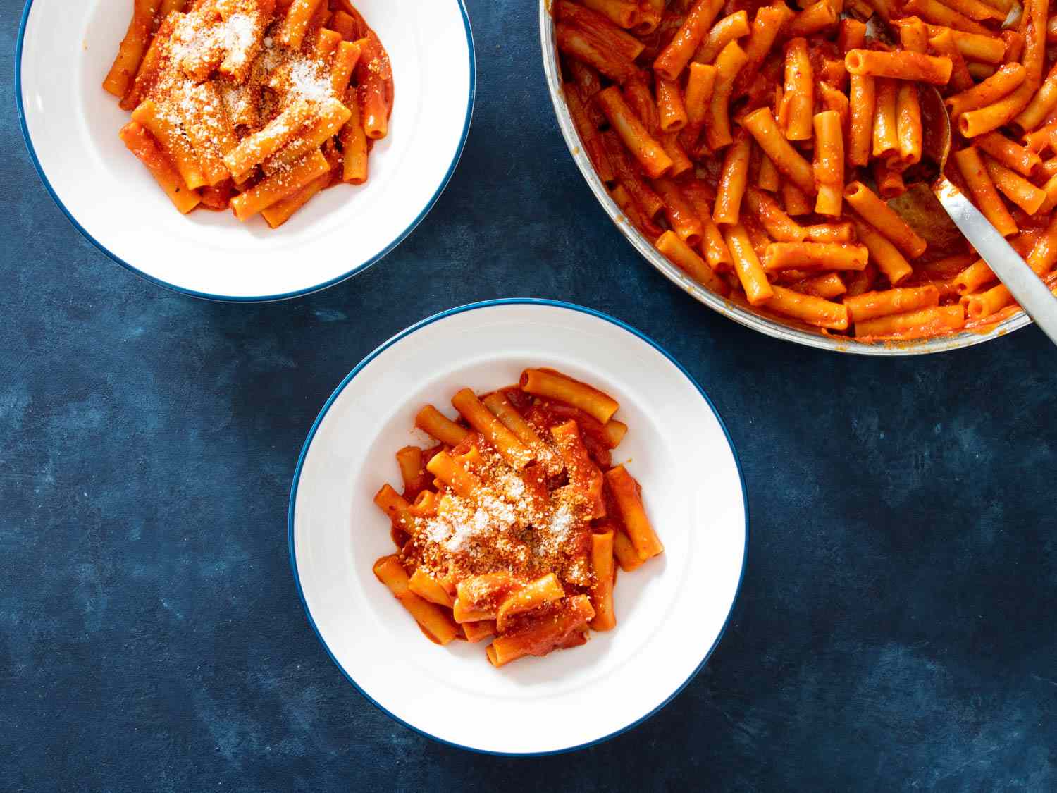 Overhead shot of two white bowls filled with pasta with tomato sauce next to a pot of pasta.