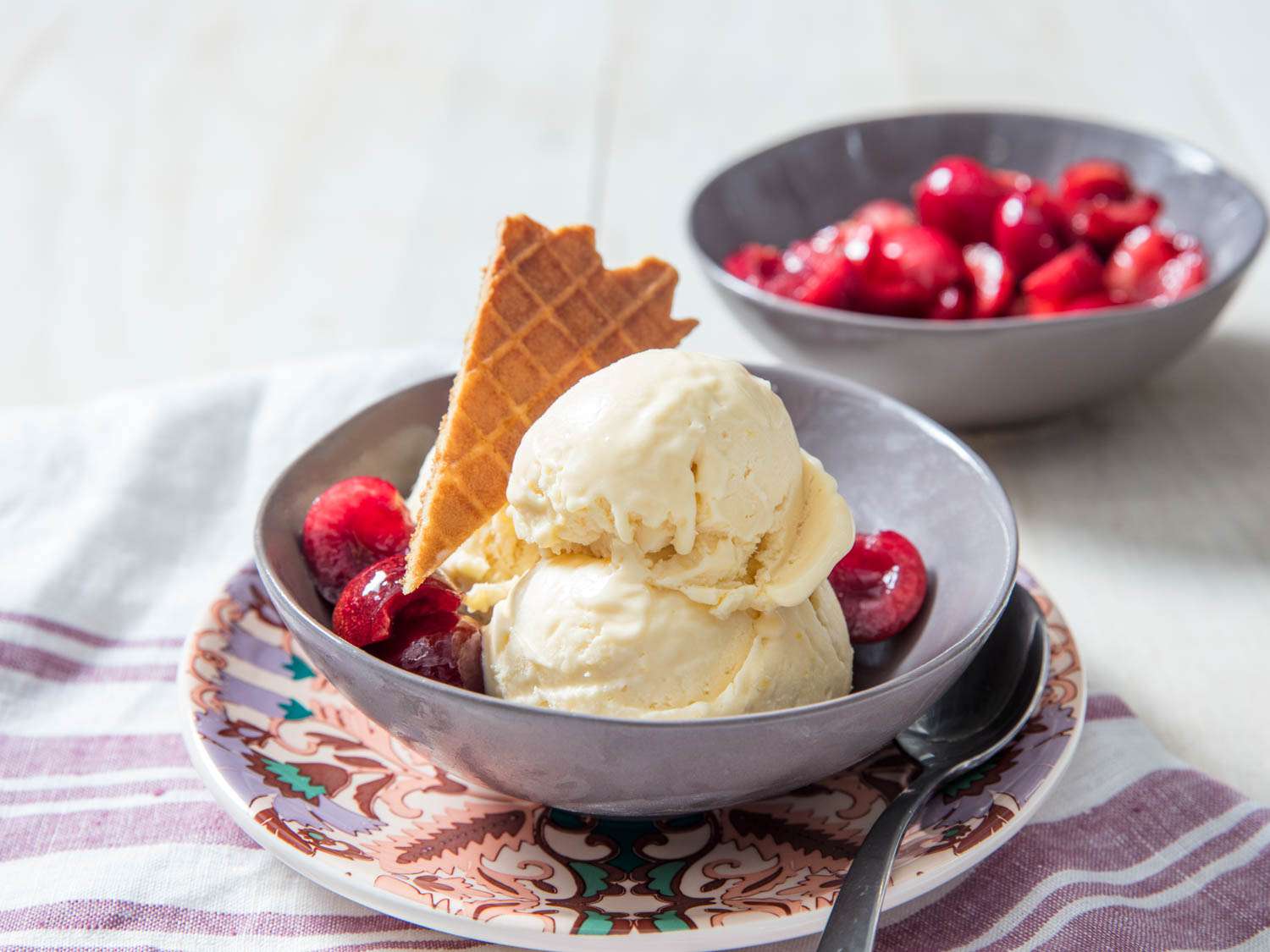 No-churn mascarpone ice cream in a purple bowl with a piece of waffle cone and cherries.