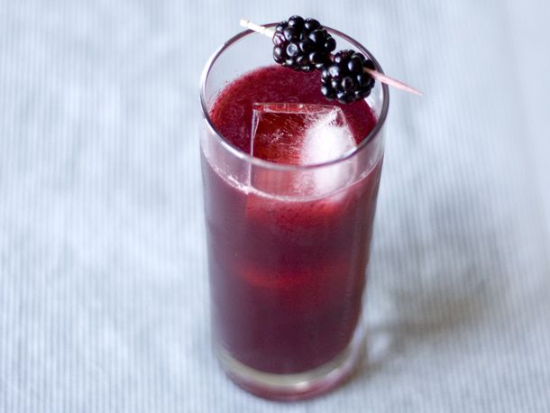 A collins glass filled with ice and a blackberry gin and tonic, garnished with two whole blackberries on a toothpick.
