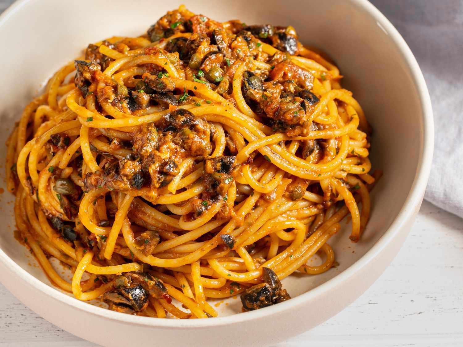 Closeup of spaghetti puttanesca, served in a white bowl.