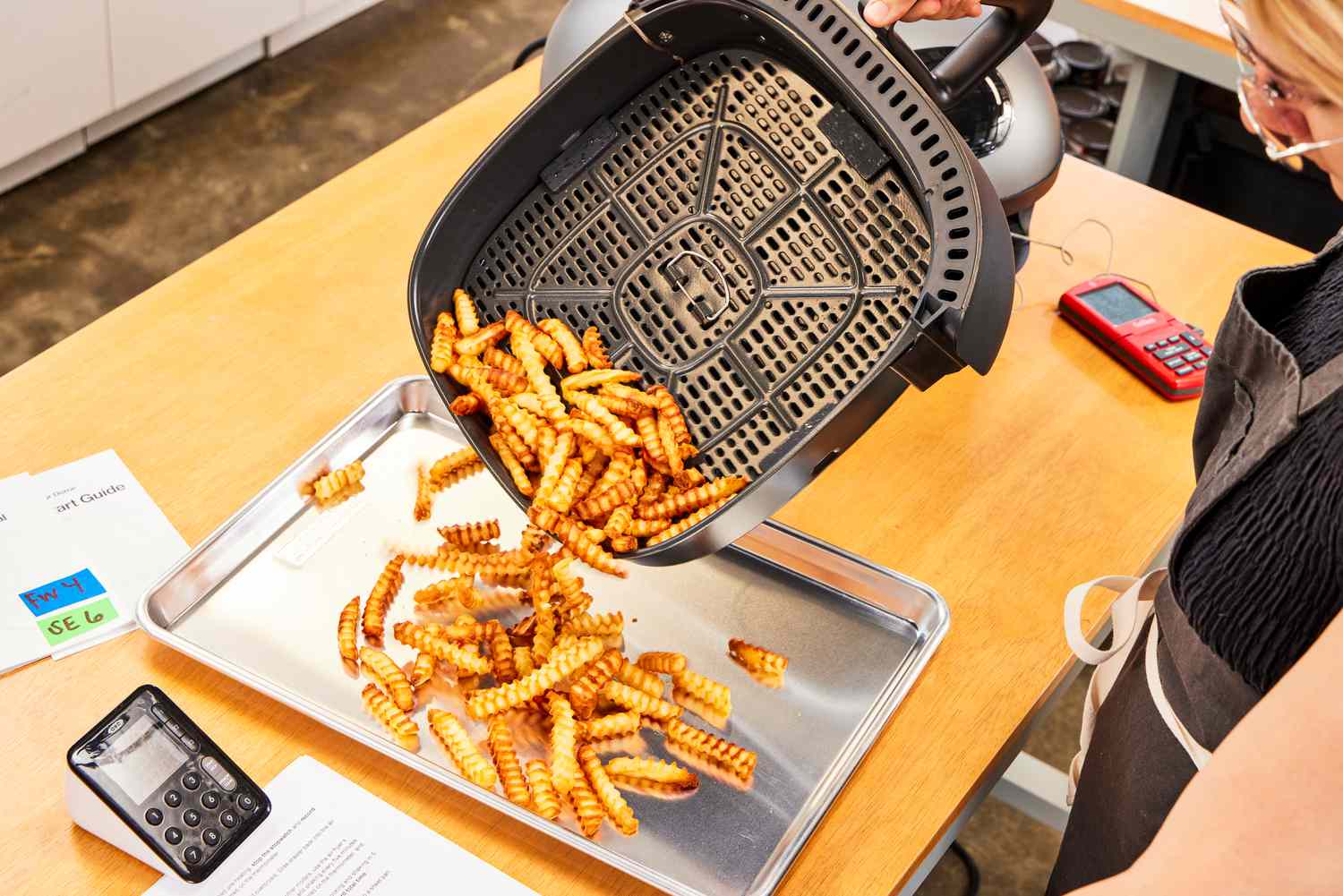 A person pouring fries from the Typhur Dome air fryer basket onto a sheet pan.