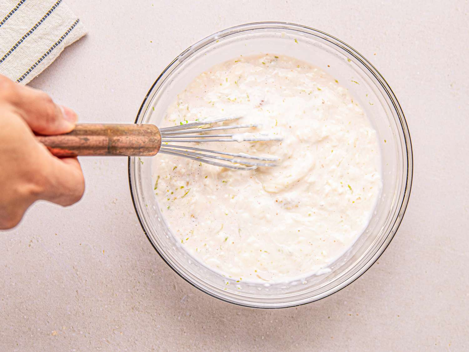 A hand whisking a creamy mixture in a glass bowl likely a salad preparation step