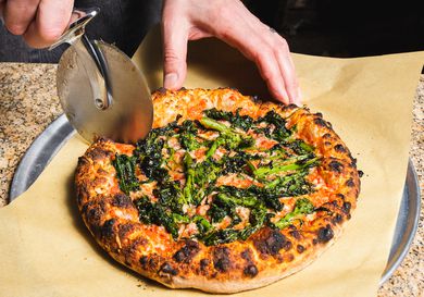 Slicing a pizza with charred broccoli rabe