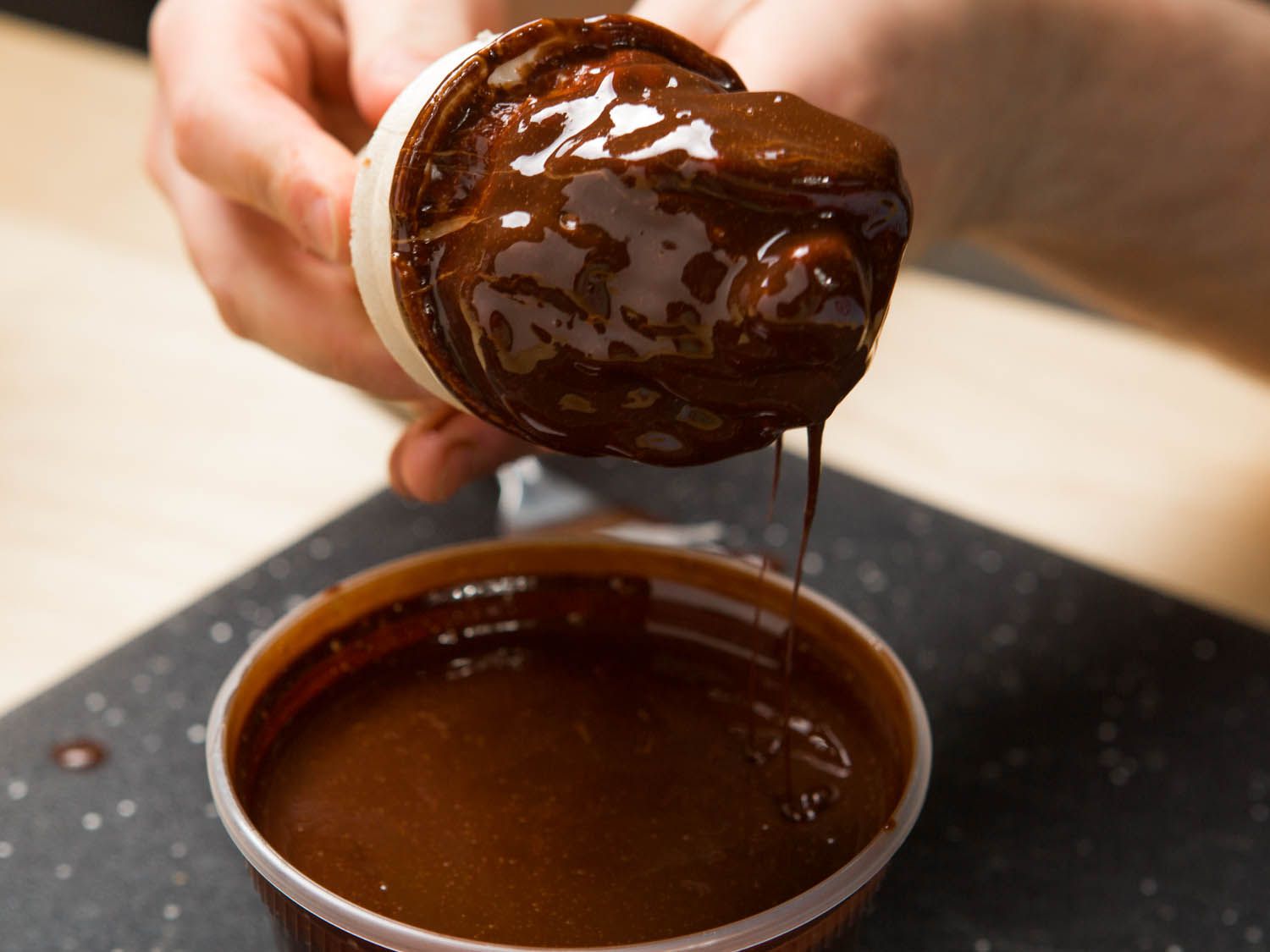 Hand rotating ice cream cone to let excess chocolate coating drip off.