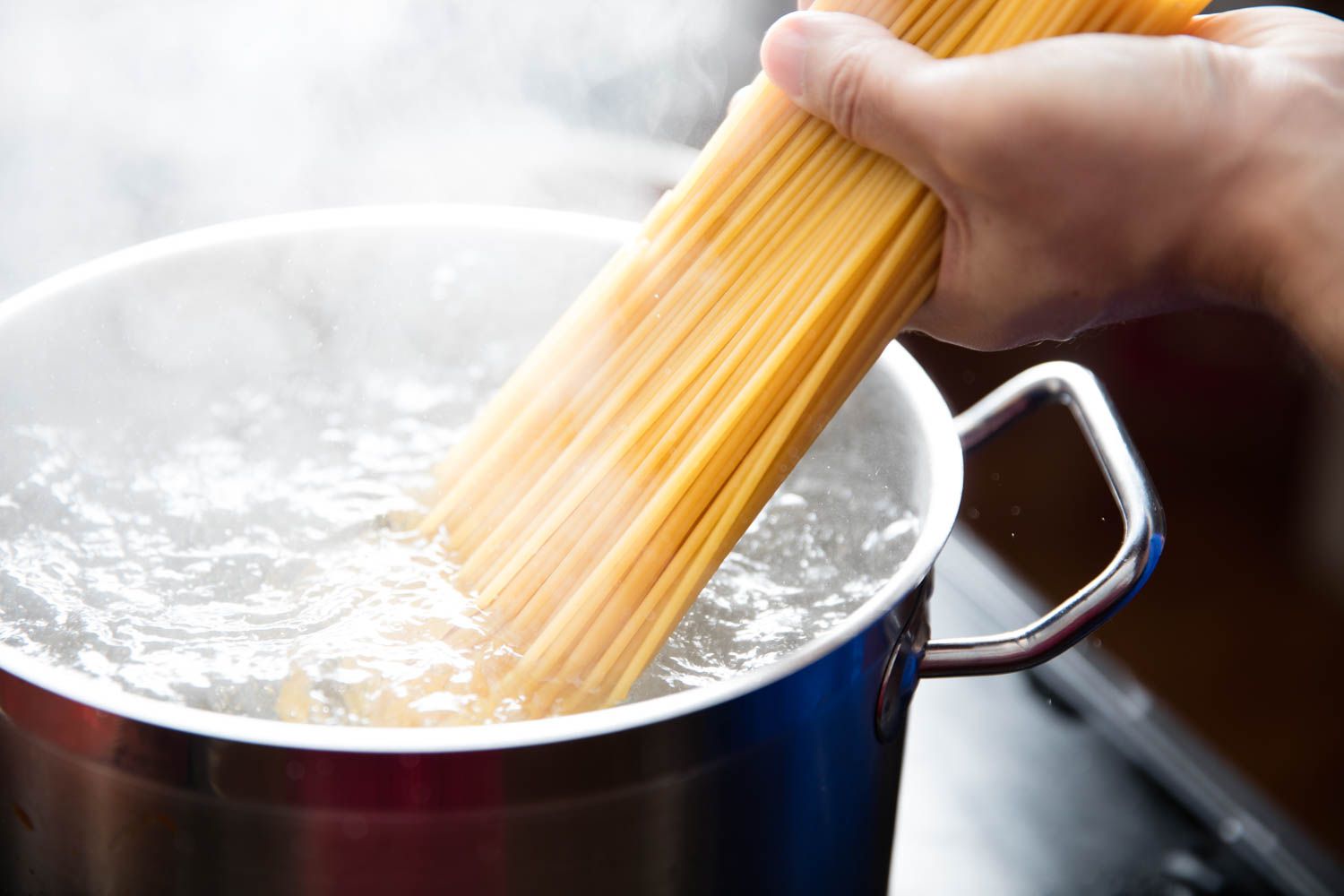 Spaghetti noodles being placed in a boiling pot of water. 