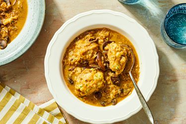 Bowl of mushroom soup with dumplings presented on a table setting including a striped napkin and drinking glasses