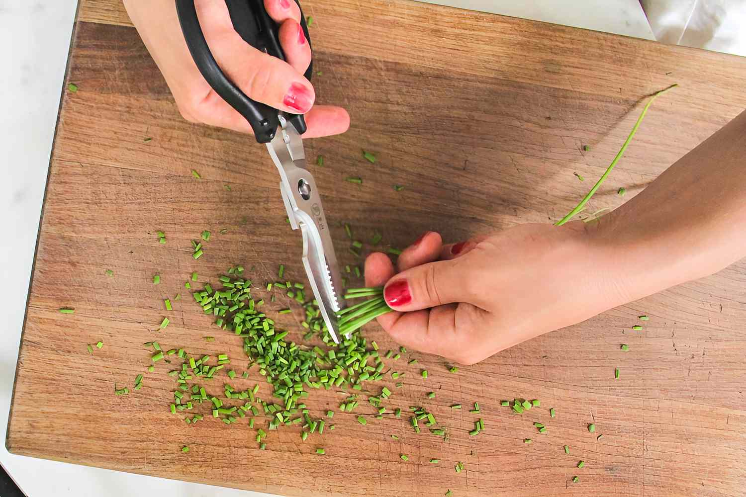 Person cutting green herbs on a wooden cutting board with kitchen scissors