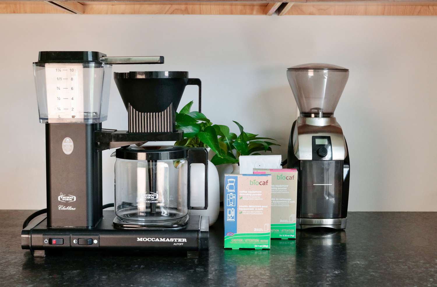 A coffee maker sitting next to two packages of descaler and cleaner and a burr grinder