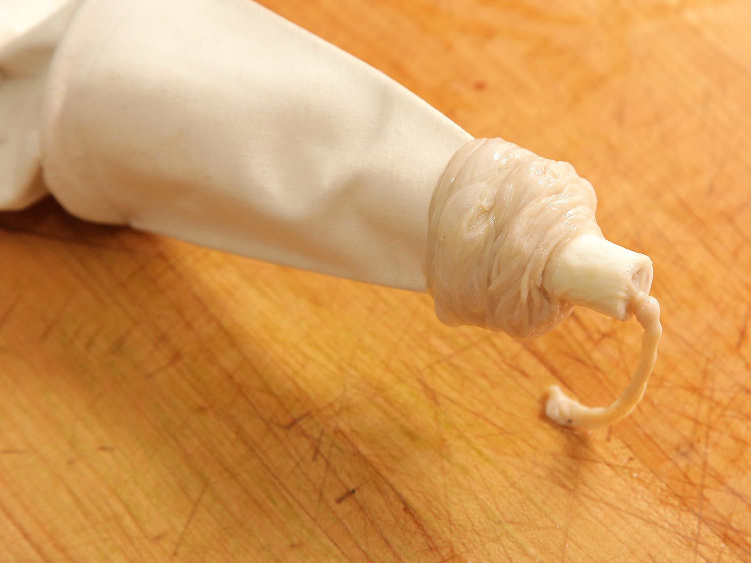 A tied sausage casing has been placed over the tip of a pastry bag.