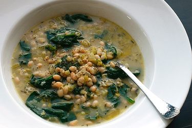Closeup of hearty white bean and spinach soup with rosemary and garlic in a wide white bowl.