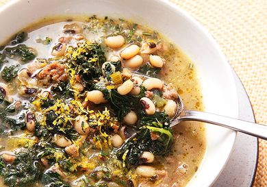 Close up view of a sausage and kale soup with peas. 