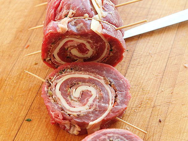 A piece of rolled flank steak stuffed with white cheese cut off the larger roll with skewers sticking through