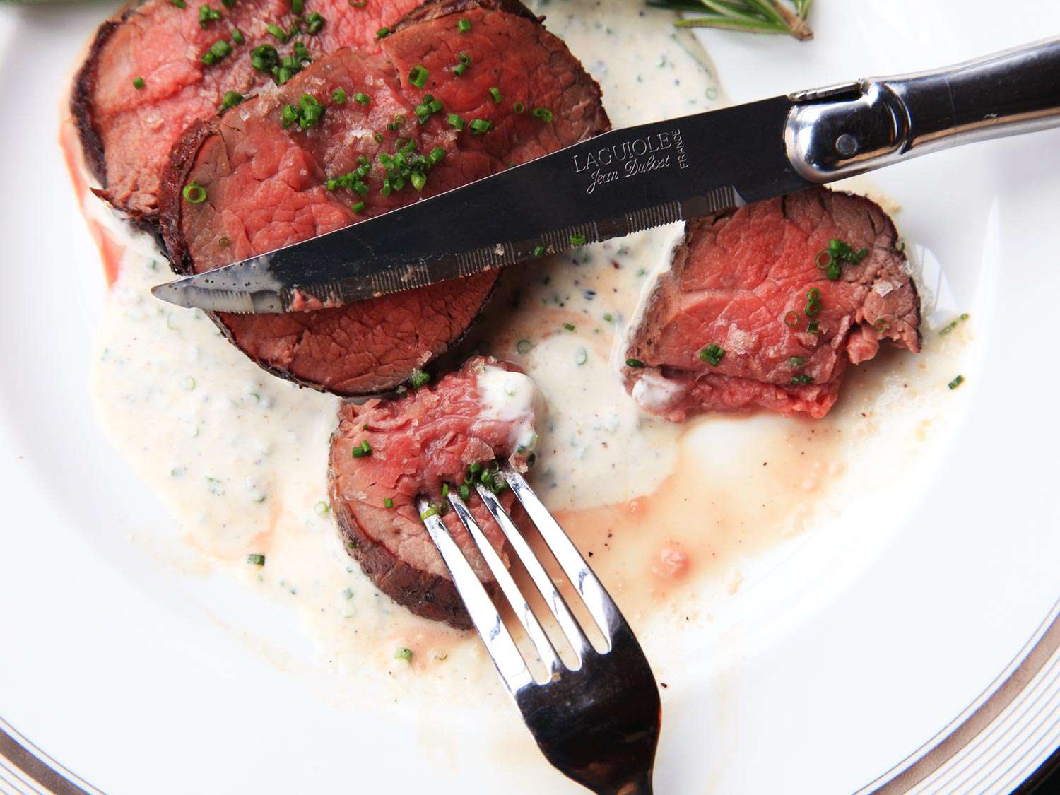 Fork and knife alongside sliced beef tenderloin medallions on a horseradish cream sauce