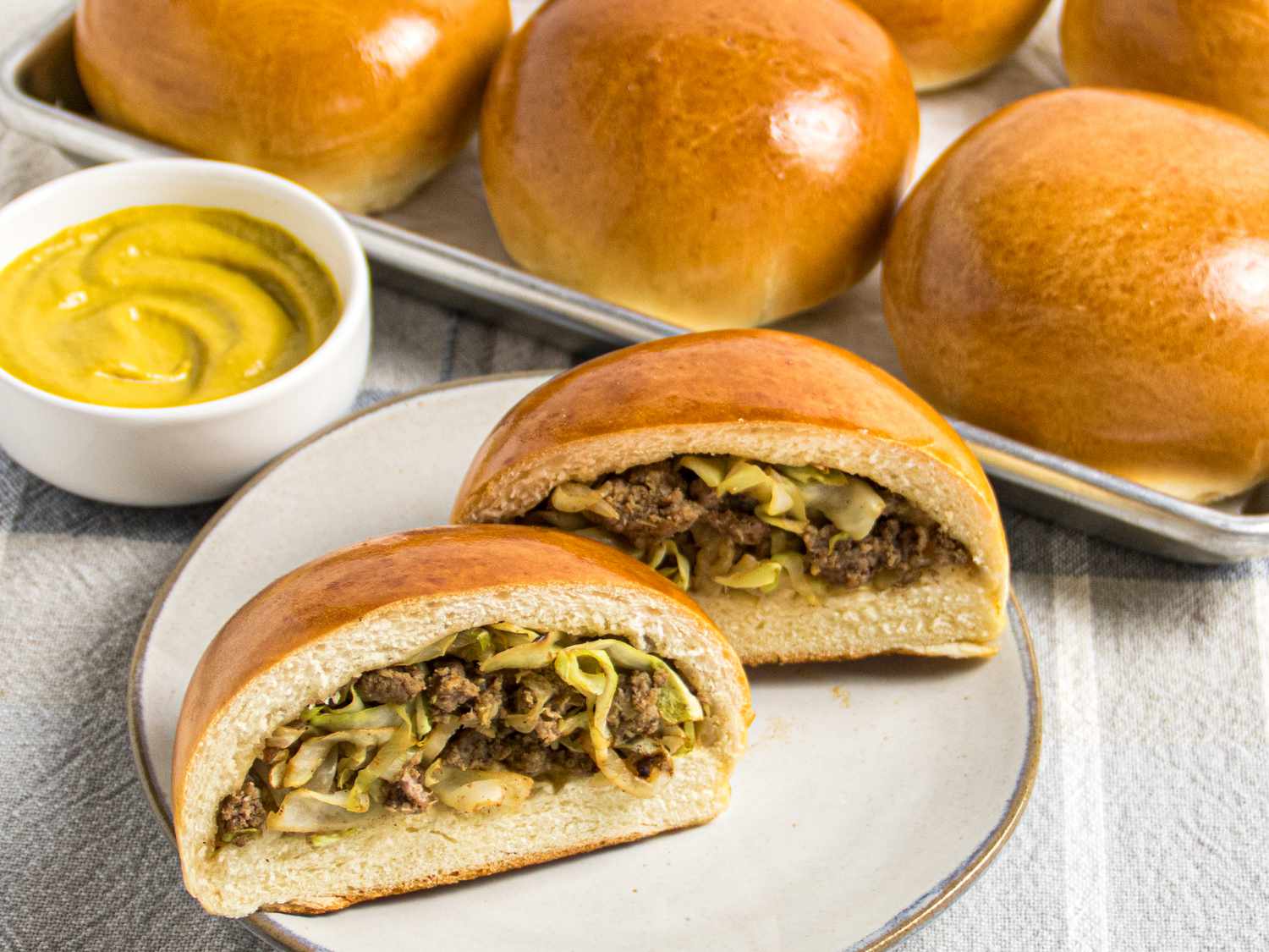 Beirock bun sliced open on a plate, with small dish of mustard, and 6 buns on a platter behind it. 