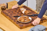 Sliced roasted meat on a Yes4All Teak Cutting Board with knife and a persons hands visible
