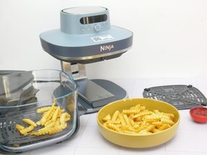 A Ninja Crispi Pro air fryer with cooked crinklecut fries in a glass container and a yellow bowl