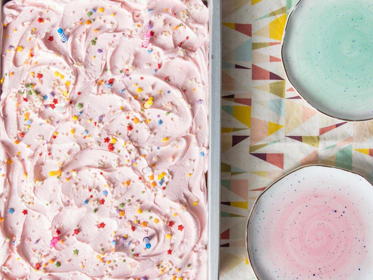 A sheet of cake iced with pink American buttercream and sprinkles.