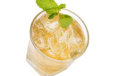 A glass of whiskey smash garnished with a fresh mint sprig.