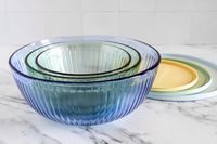Stacked tinted glass mixing bowls with lids on a marble surface